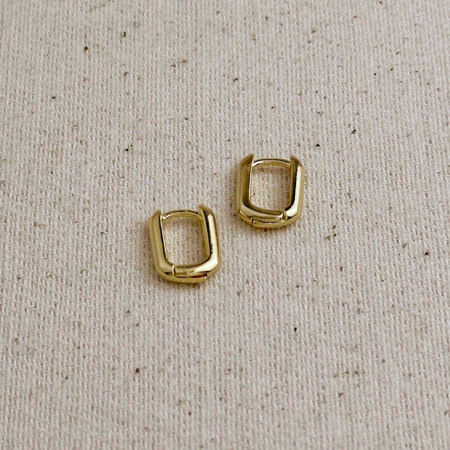 Oblong gold filled hoop earrings on a beige fabric background