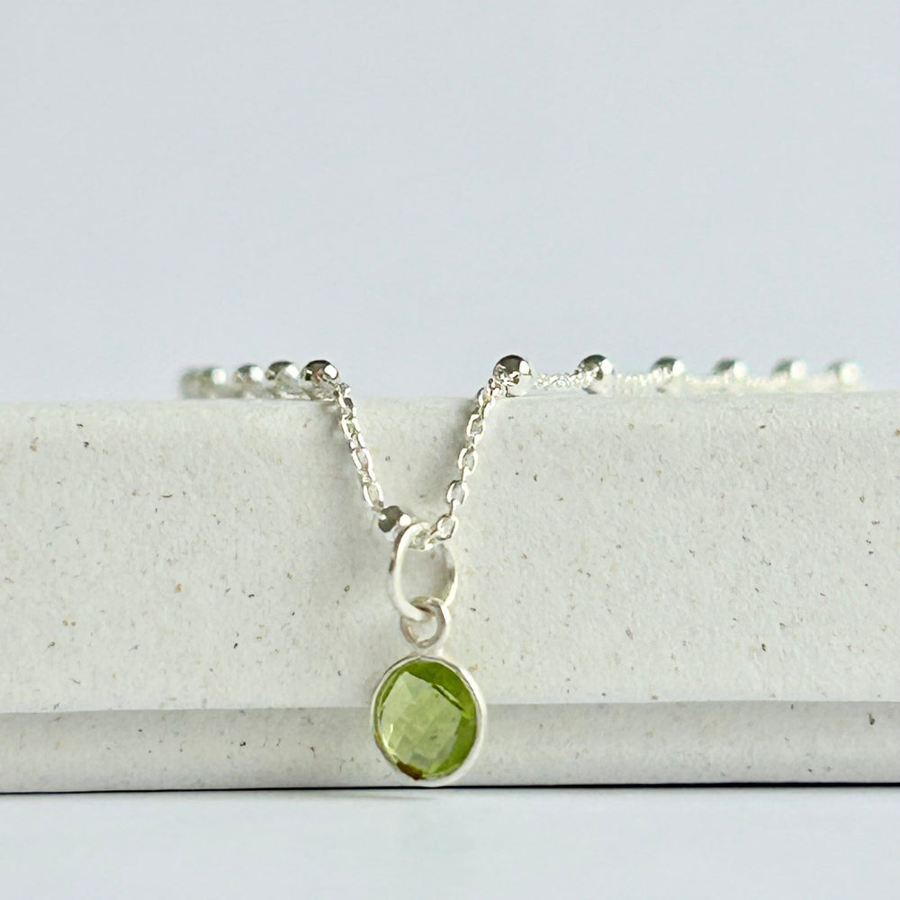 Silver necklace with a vibrant green peridot pendant, resting on a white box.