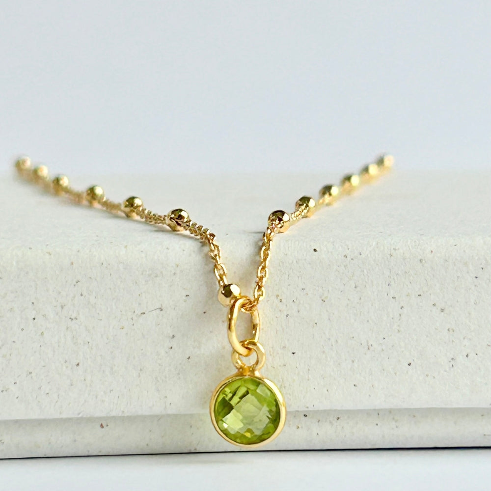 Gold necklace with a vibrant green peridot pendant, resting on a white box.