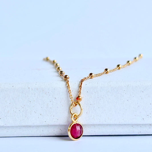 Gold necklace with a tuby pendant resting on a white box