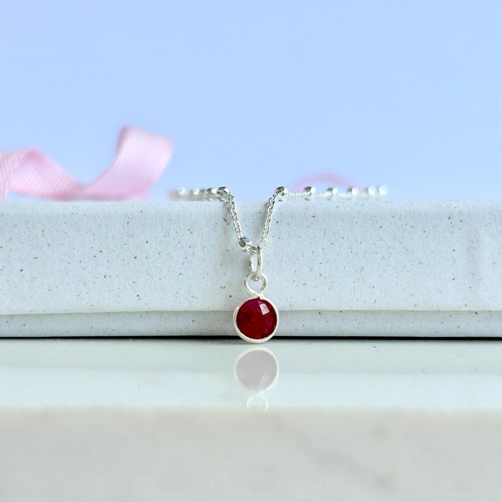 Sterling silver chain with a ruby pendant, resting on a white box