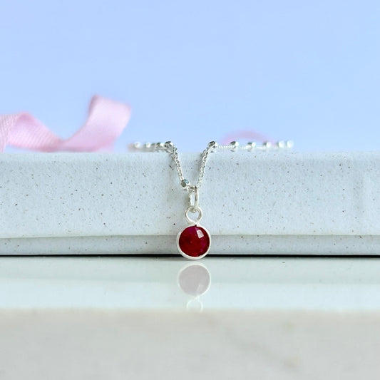 Sterling silver chain with a ruby pendant, resting on a white box