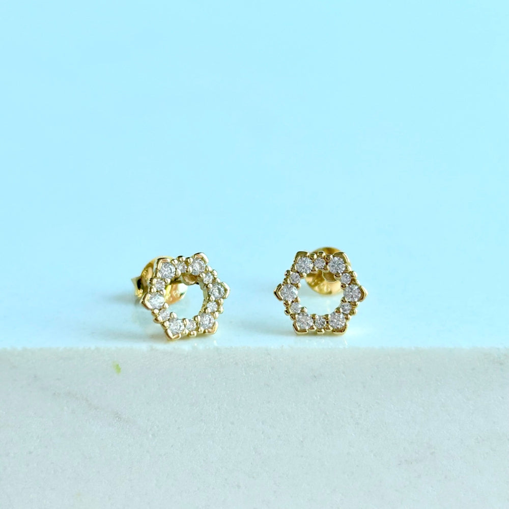 A pair of gold-colored hexagon stud earrings adorned with sparkling cubic zirconia stones, displayed against a light background.