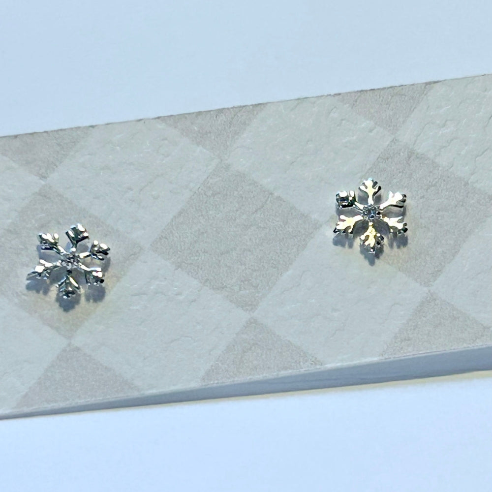 Sterling silver snowflake stud earrings with a single sparkly stone, on a textured presentation card.