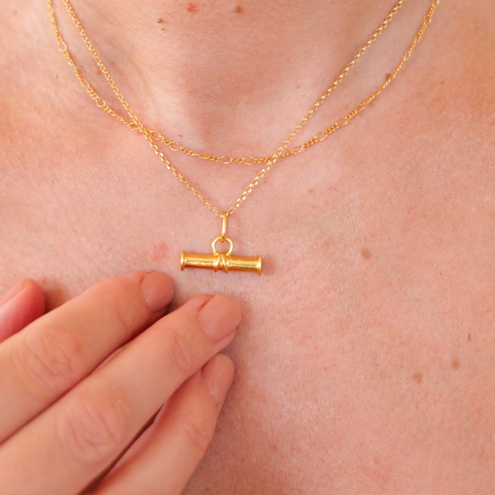 Gold t-bar necklace and figaro chain on a person's neck