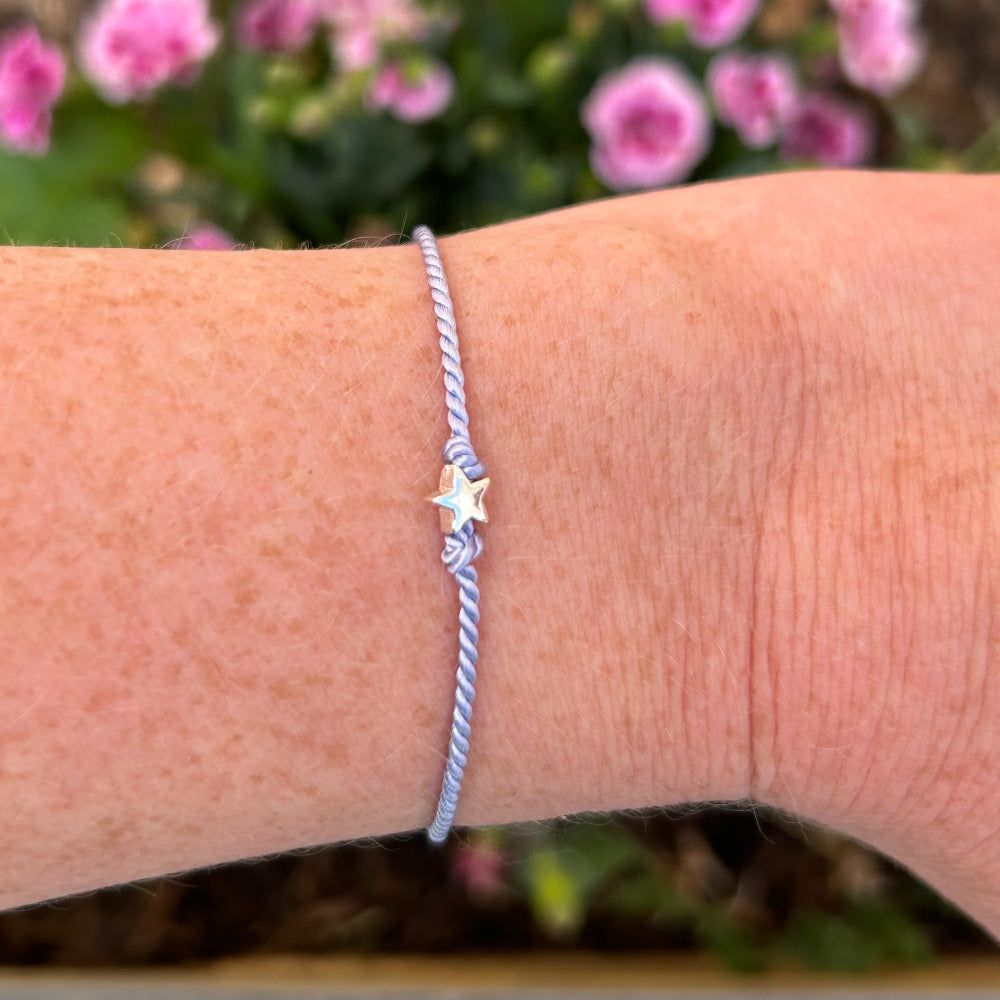 A lilac silk friendship bracelet with a star charm on a wrist
