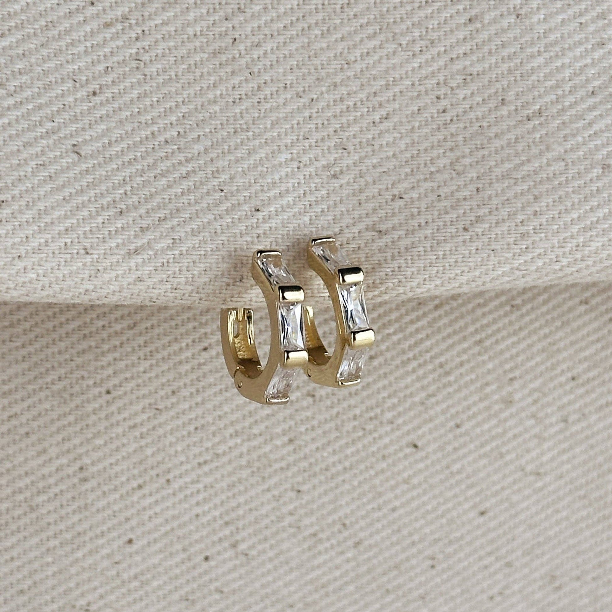 Gold hoop earrings with clear baguette cut cubic zirconia stones on a textured beige background