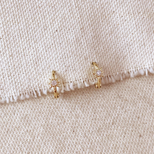 Pair of gold hoop earrings with sparkly starburst designs on a beige fabric background