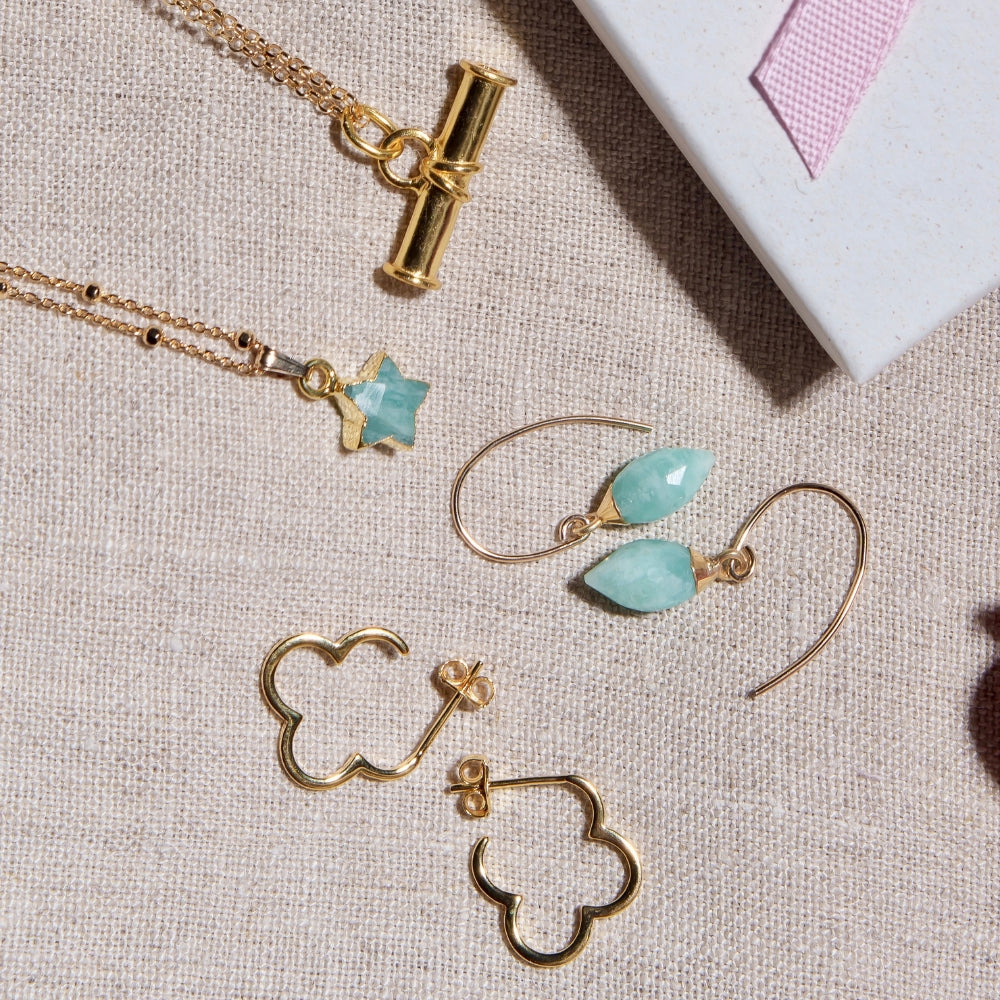 Gold and turquoise (amazonite) jewellery, including a t-bar nacklace, amazonite star necklace, amazonite drop earrings and gold clover hoop earrings on a textured surface.