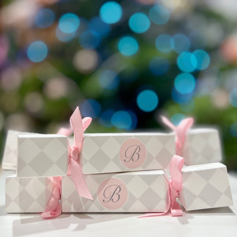 Two harlequin design crackers tied with pink ribbons on a blurred bokeh Christmas tree background