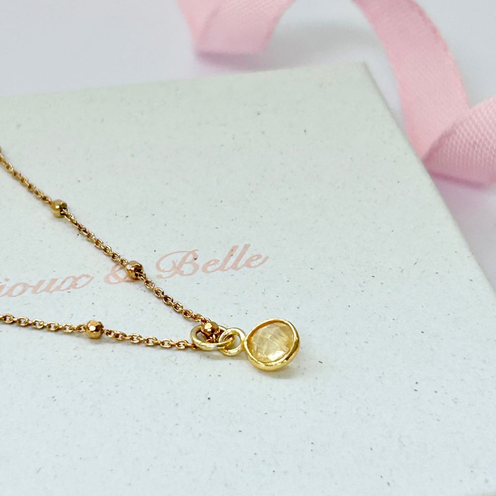 A gold satellite chain necklace with a warm yellow citrine pendant, resting on a box branded 'Bijoux & Belle'.