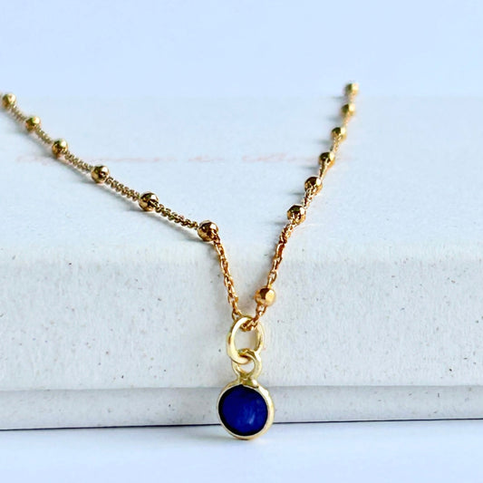 Blue sapphire pendant on a gold satellite chain, resting on a white box.
