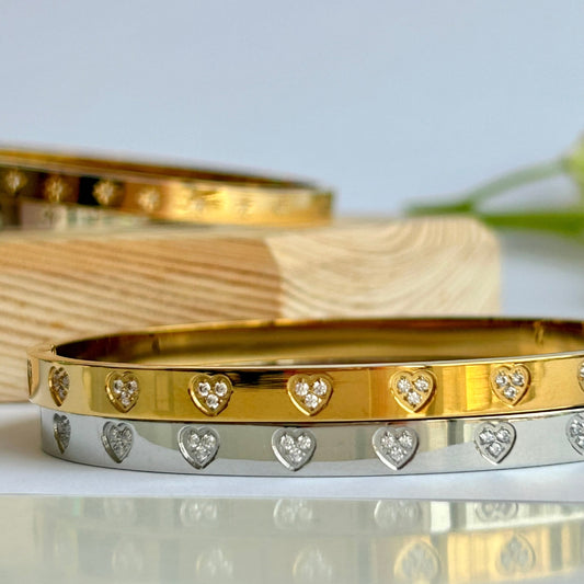 Gold and silver bangles stacked on top of each other with sparkly heart designs on a reflective surface.