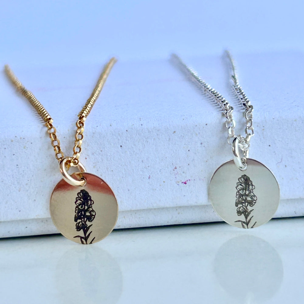 Two necklaces with floral engraved pendants (July birth flower) on a light blue background