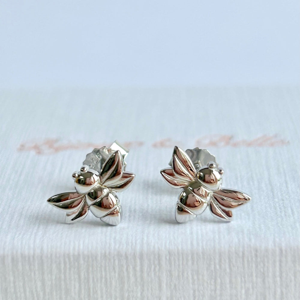A pair of silver bee-shaped stud earrings resting on a textured white jewellery box branded with 'Bijoux & Belle'.