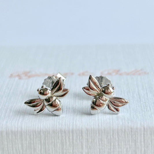A pair of silver bee-shaped stud earrings resting on a textured white jewellery box branded with 'Bijoux & Belle'.
