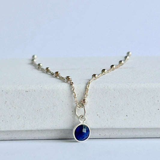 Blue sapphire pendant on a sterling silver satellite chain, resting on a white box.