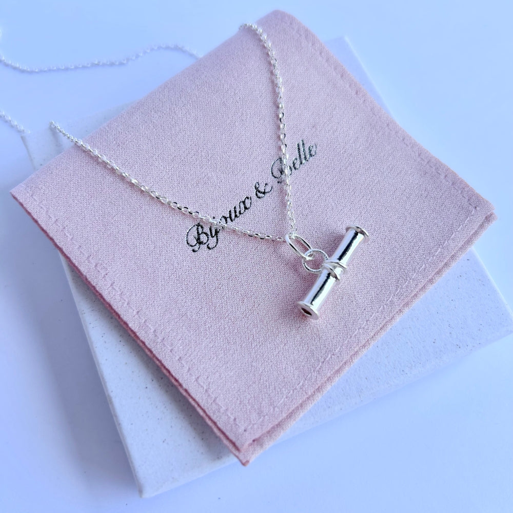 Silver t-bar necklace on a pink jewellery pouch with Bijoux & Belle branding.