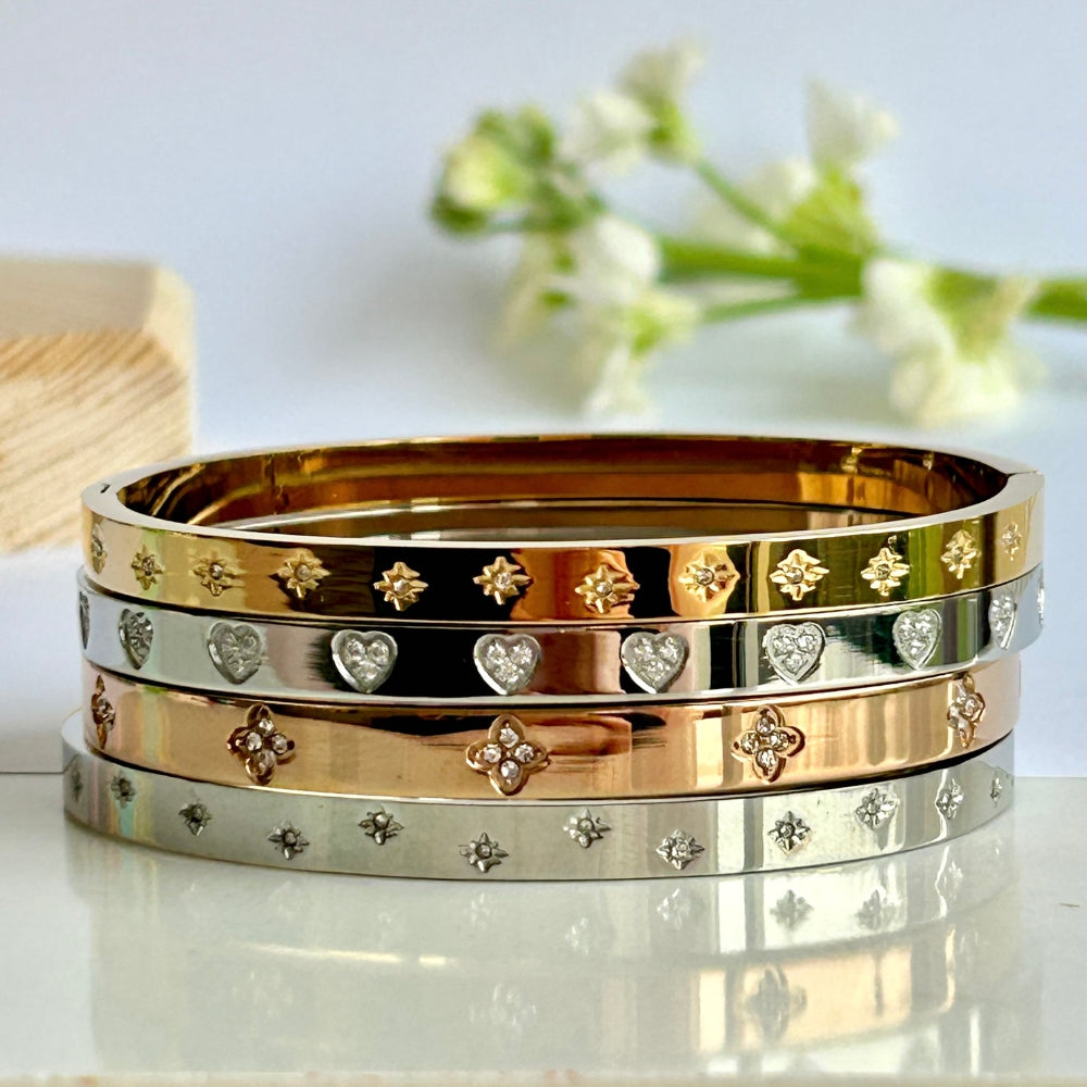 Stack of gold, silver, and rose gold bangles with decorative patterns on a reflective surface.