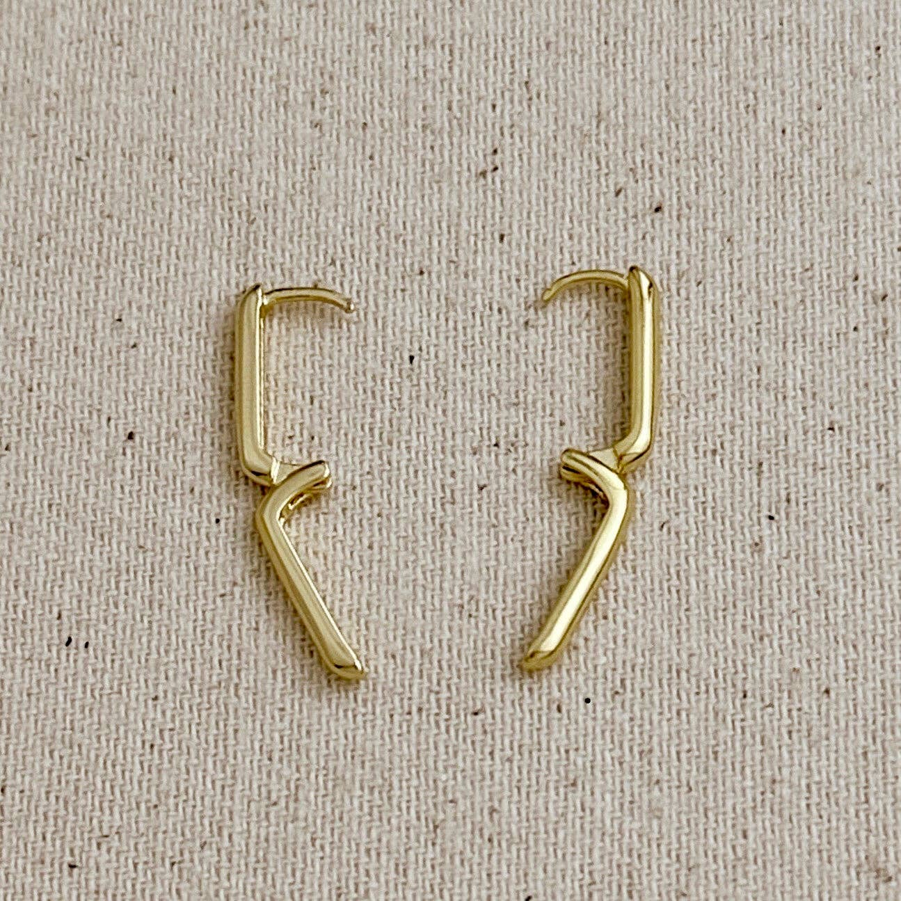 Open gold filled hoop earrings on a beige fabric background.