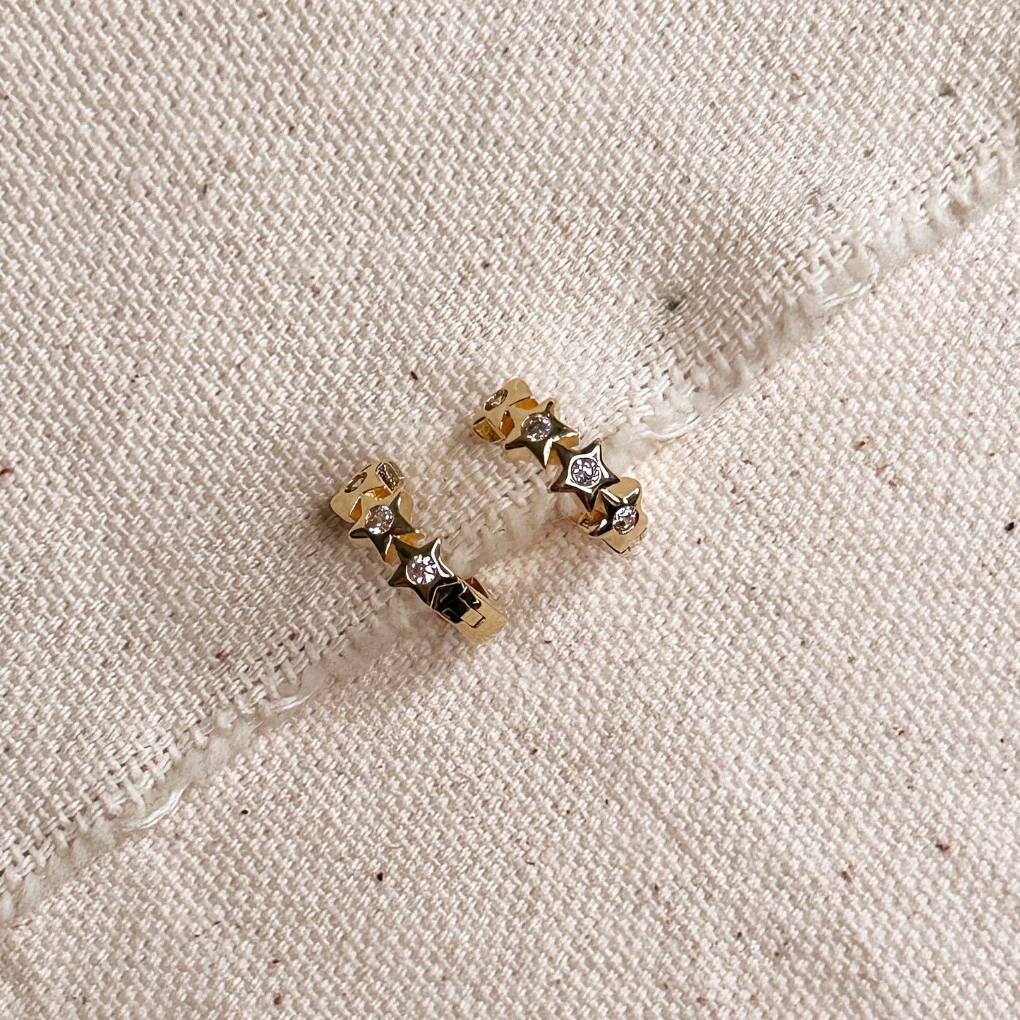 Pair of gold hoop earrings with star designs on a textured beige surface.  Each star has a centre crystal.